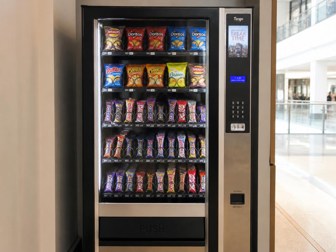 Snack vending machine stocked with chips and chocolate bars in a shopping centre walkway